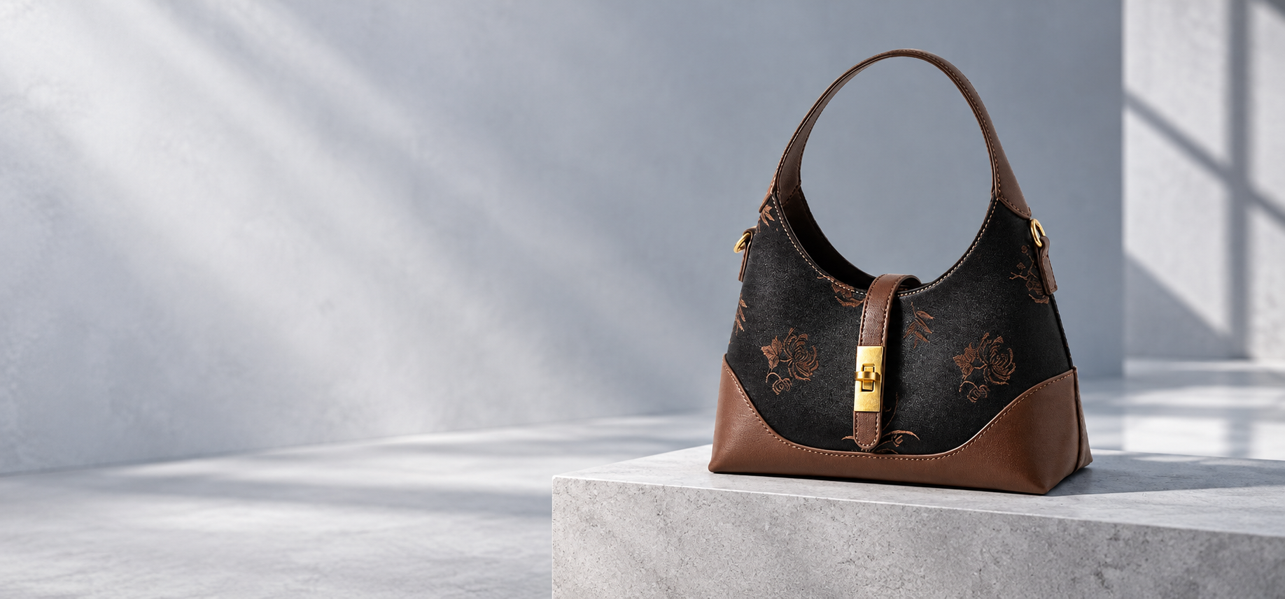 Black botanical handbag with brown trim and gold clasp, displayed on a stone plinth.